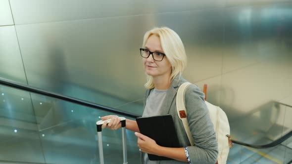 Business Woman with Travel Bag and Tablet Rides on the Escalator in the Airport Terminal or Subway