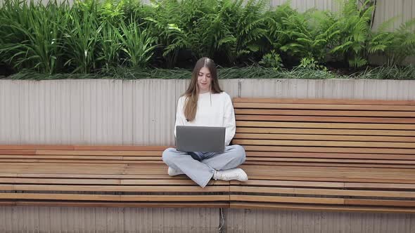 Young Female in Garden Using Laptop Communicates on Internet with Customer