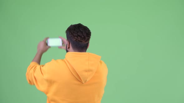 Rear View of Young Overweight Bearded Indian Man Taking Picture with Phone alt