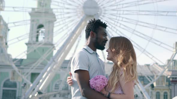 Young Interracial Couple Hugging Near Ferris Wheel in the City alt