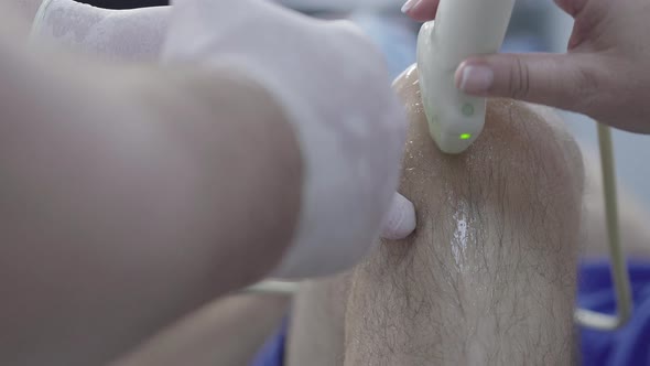 Extreme Close-up of Doctor Inserting Syringe Into Male Knee and Using Ultrasound Equipment alt