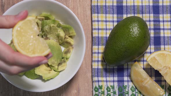 Guacamole Recipe, Second Step. The Lemon Is Squeezed Into the Avocado Pulp in a White Plate, Then