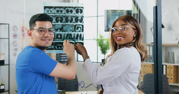 Mixed Race Doctors Posing on Camera During Examining Results of X-ray Image Attached to Glass Board alt