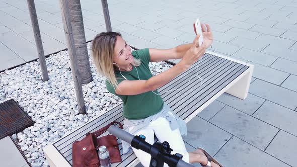 Woman sitting on bench in city having video call over smartphone
