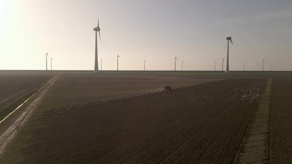 Orbiting around Tractor working on land followed by seagull, Windmill farm Background alt