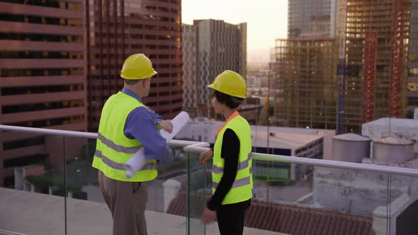 Two construction supervisors look at plans on rooftop
