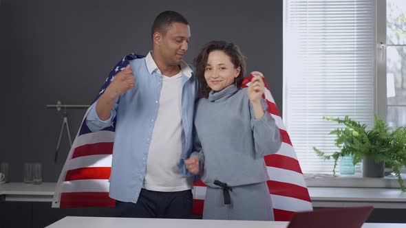 Portrait of Happy Interracial Couple Posing with USA Flag in Kitchen at Home alt