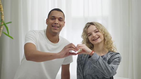 Medium Shot of Happy Smiling Interracial Couple Making Heart Shape with Hands Smiling Looking at alt