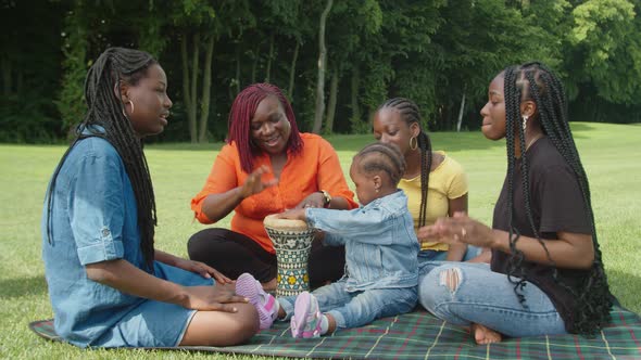 Joyful Black Mom and Cute Daughters Playing Ethnic Music on Traditional African Hand Drum Djembe alt