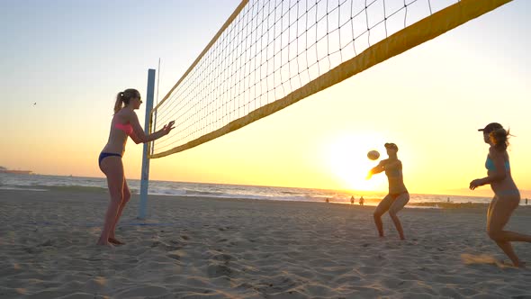 Women players play beach volleyball and a player hitting spiking the ball. alt