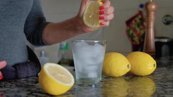 Woman squeezing lemon with both hands on glass with ice between lemons alt