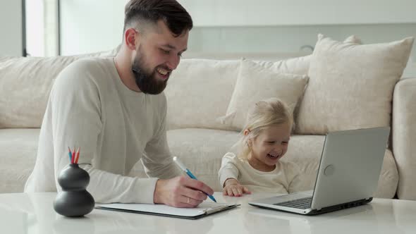 Young Father Teaches a Young Daughter Using a Laptop Near the Sofa in the Living Room of the House alt
