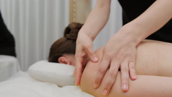 Female therapist massages a young woman on her back and shoulders. Relaxing massage.