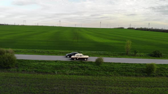 Beautiful Retro Sedan of Beige and Burgundy Rides on Road in Green Field alt