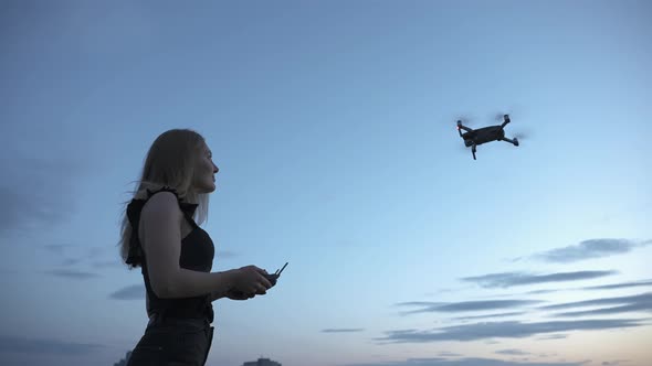 Young girl controlling quadcopter drone flying in the air with remote controller under blue sky in t alt