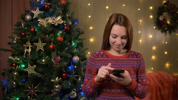 Beautiful Woman Near Decorated with Christmas Tree Using Smartphone