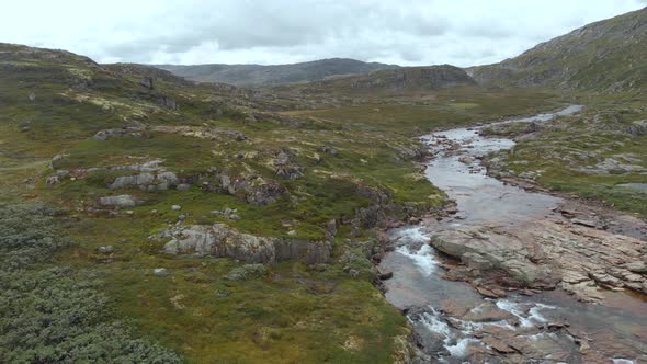 Meltwater river flowing in Norway Hardangervidda valley, aerial side truck view alt