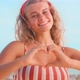 Young Happy Caucasian Woman Making Shape Heart Gesture Smiling Stands on Beach - VideoHive Item for Sale