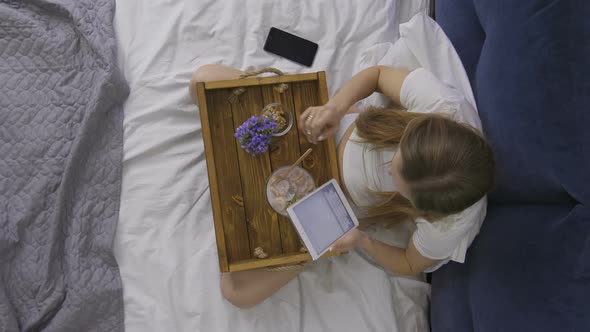 Woman Eating Breakfast and Using Touchpad alt