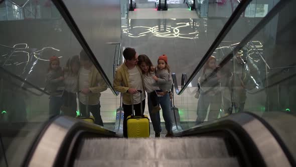 Happy Young Family with Yellow Suitcase Going Up By the Escalator From the Airport Hall alt