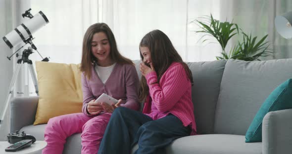 Happy girls sitting on the sofa and connecting with a digital tablet