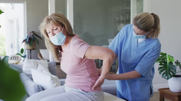 Female health worker stretching back of senior woman at home alt