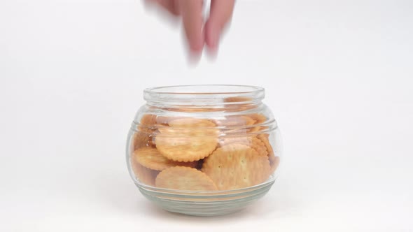 Hand picking Biscuits cookies in a glass jar on white background.