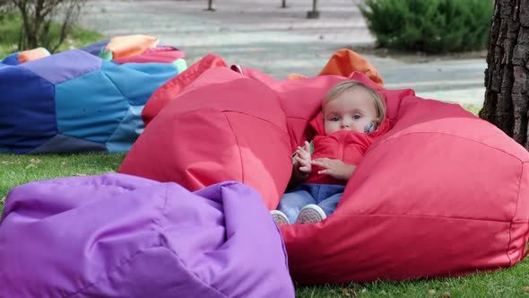 Little cute girl sits on the large soft garden chair on playground in the park. Slow motion.