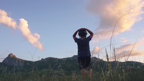 a Boy in a Helmet Looks at a Mountain Range in the Sunset