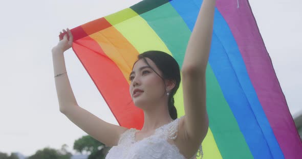 Asian Lesbian Girl Raising LGBT Rainbow Flag In The Park. alt