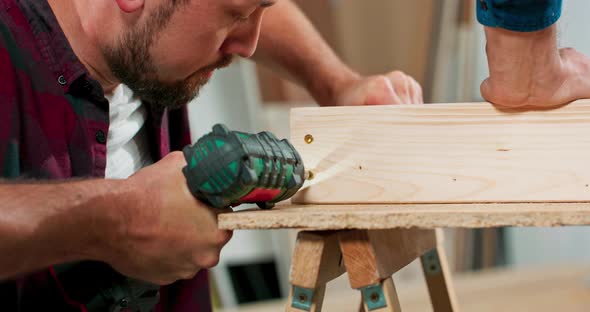 Concentrated Young Bearded Passionate Carpenter Drives a Carpentry Screw Into a Construction Beam alt