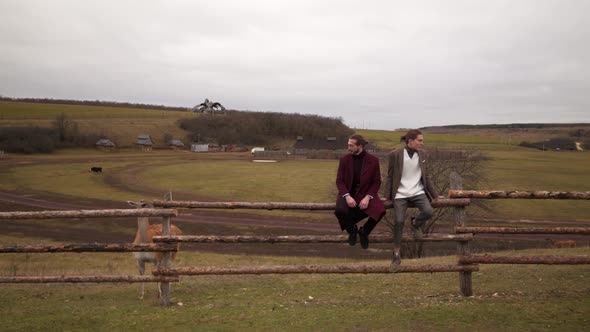 Two Men Stand Near the Fence of an Agricultural Farm in Classic English Clothing