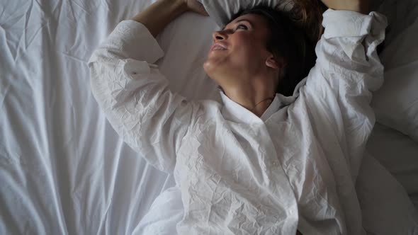 a Brunette Woman Lies on a White Sheet and Throws Up a Pillow