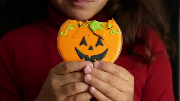 Halloween. Little girl bites pumpkin-shaped gingerbread. Halloween sweets and treats.