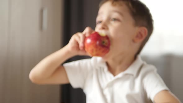 A Cute Boy Takes a Red Apple and Eats It, Experiencing Emotions of Happiness, Joy and Laughter alt