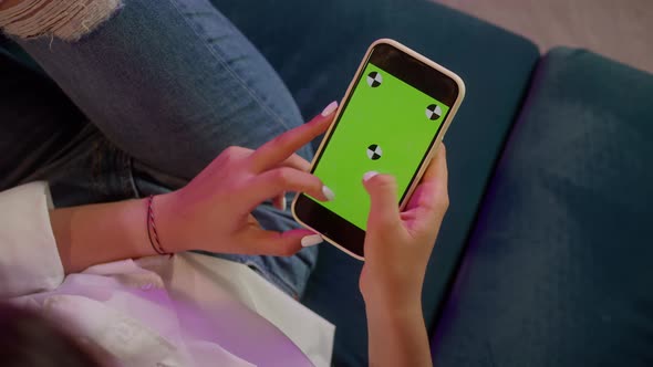 Young Woman Sitting on Sofa and Holding Smartphone with Chroma Green Screen Closeup Surfing the alt