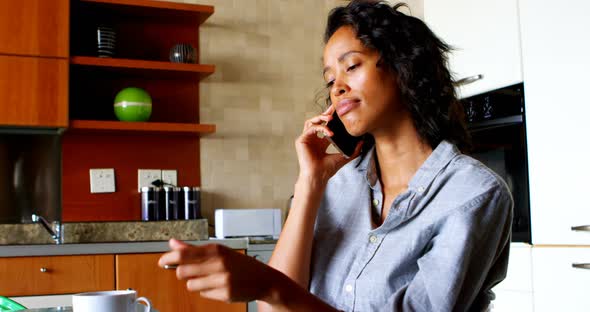 Woman with coffee cup talking on mobile phone in kitchen 4k alt