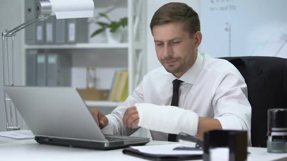 Workaholic Man With Broken Arm in Gypsum Typing One Hand on Laptop Pc, Trauma