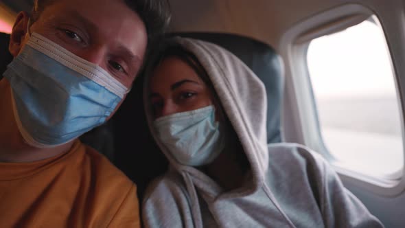 Happy Couple Man and Woman in Medical Safety Mask at Aircraft Cabin Next to Window at Take Off alt