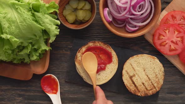 Top View of the Wooden Spoon Spreading a Tomato Sauce on the Burger Bun alt