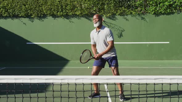 African american senior man playing tennis on the tennis court on a bright sunny day alt