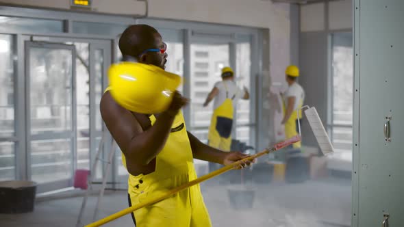 Shirtless African Builder in Overall and Hardhat Playing Guitar Using Paint Roller alt
