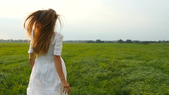 Beautiful Young Woman in White Dress Running on the Green Field. Wind Blowing Hair