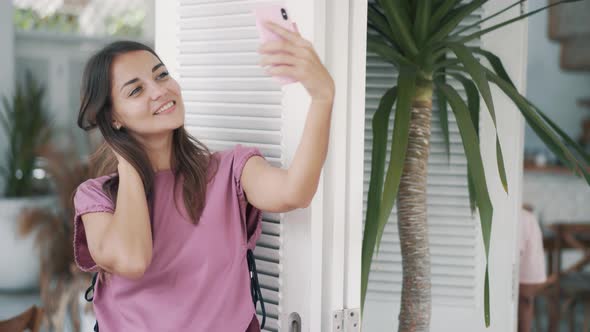 Portrait of Woman in Outdoor Cafe, Takes Selfie on Phone, Shows Peace Gesture alt