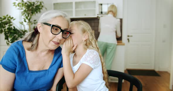 Granddaughter Whispering To Granny Indoors