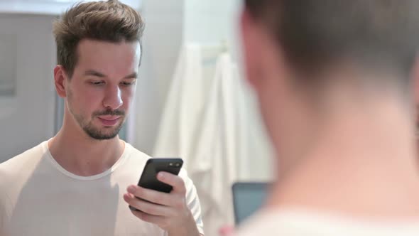 Young Man Using Smartphone in Mirror alt
