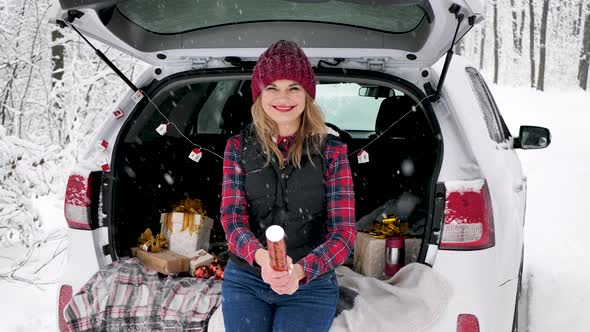 Young Beautiful Woman is Sitting in the Trunk of a Car in a Snowy Forest and Explodes a Firecracker