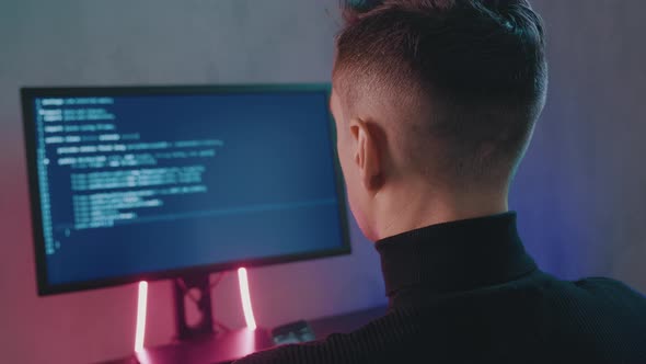 Rear View of Man Programmer Coding Network Security Software Indoors in Neon Lights. Hacker Typing alt