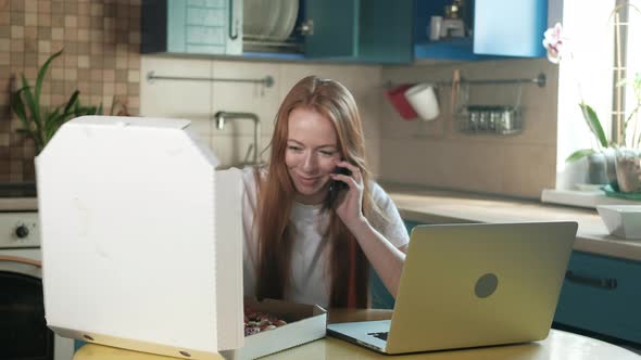 woman is talking on modern phone in kitchen slice of pizza and eats alt