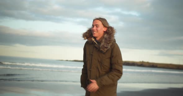 Young blond cheerful man is running along the beach alt